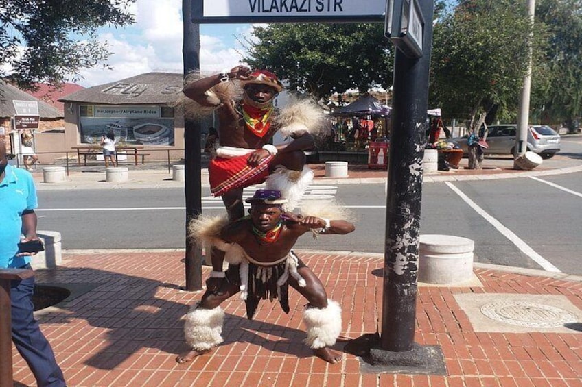 Two individuals in traditional attire performing a dance at a street corner. 1