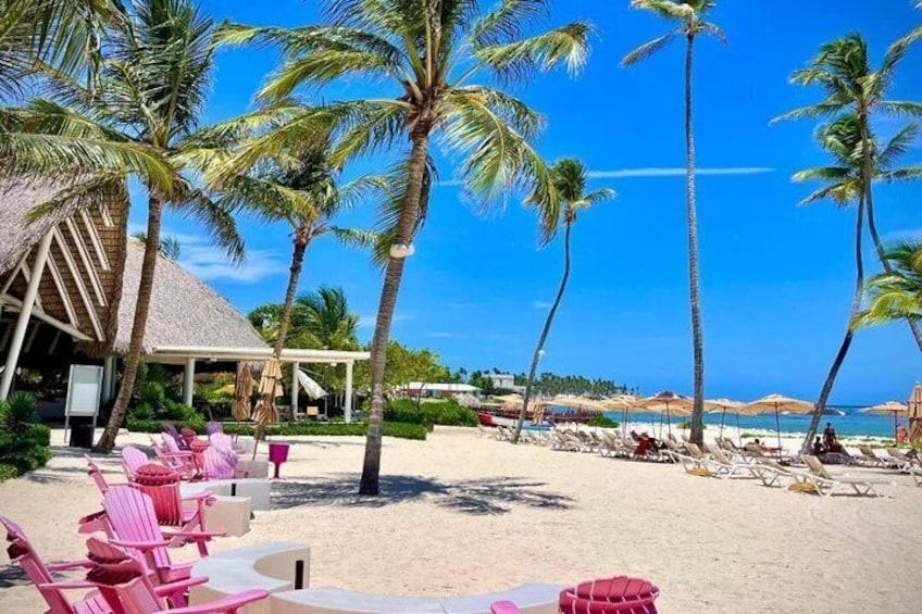 A beach with palm trees, lounge chairs, and a thatched-roof building. 1
