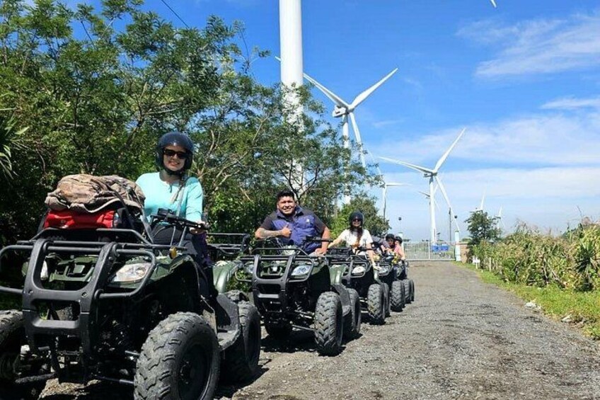 A group of people on ATVs on a gravel path with wind turbines in the background. 5