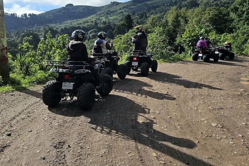 A group of people on ATVs on a dirt road with a hilly landscape in the background. 2