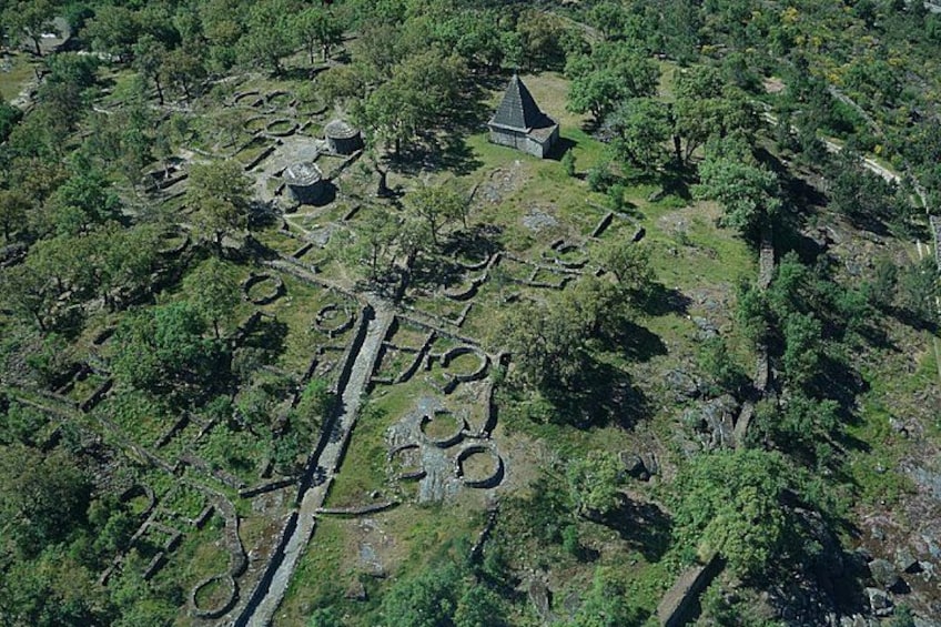 An aerial view of an archaeological site with circular stone structures and a small building. 1