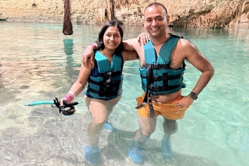 Two people in clear water, wearing life vests, with a rocky background. 2