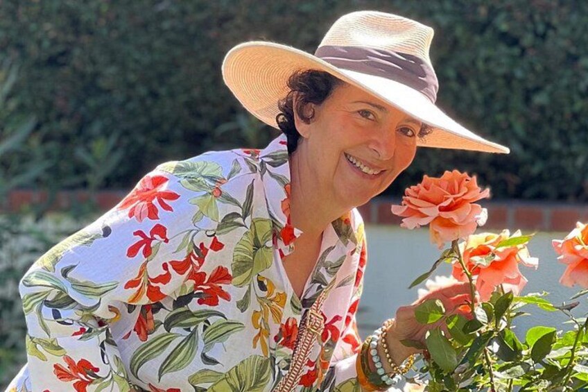 Iemand met een bloemenhemd en een ruime hoed, staat nabij een plant met oranje bloemen. 3