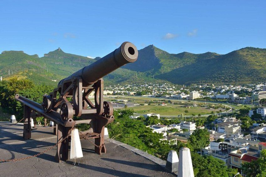 A cannon on a hill overlooking a town with mountains in the background. 4