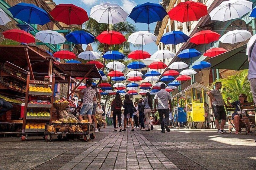 A market with colorful umbrellas, fruit stalls, and people shopping. 3