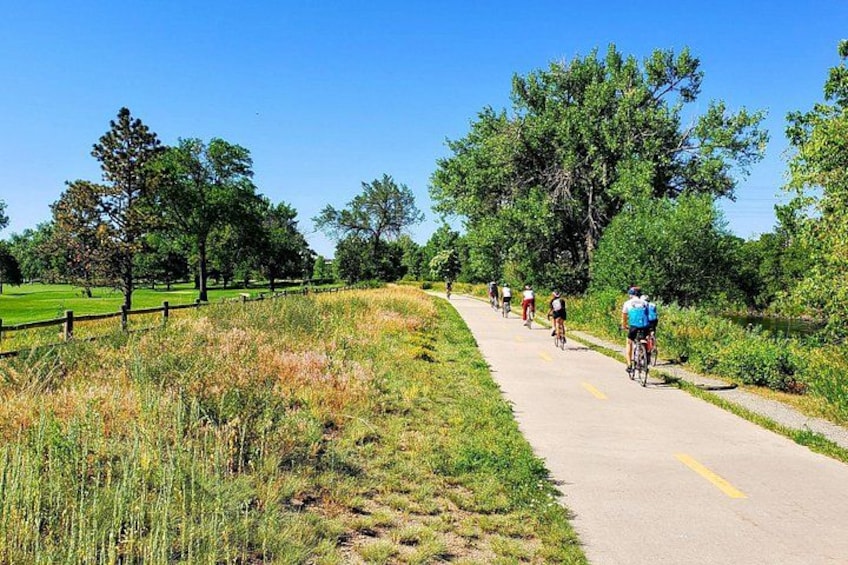 Un chemin pavé, bordé de gazon et d’arbres, où l’on peut apercevoir des cyclistes. 1