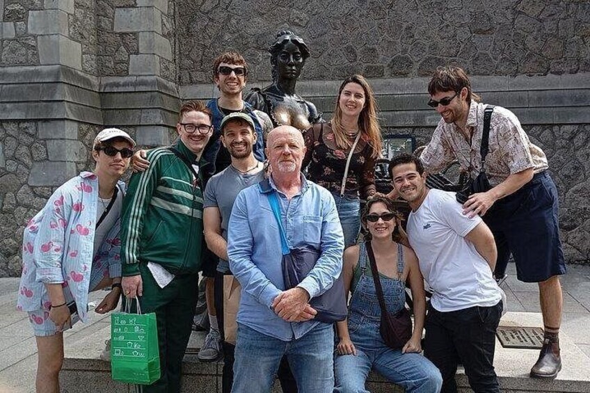 A group of people posing in front of a stone wall with a statue. 1
