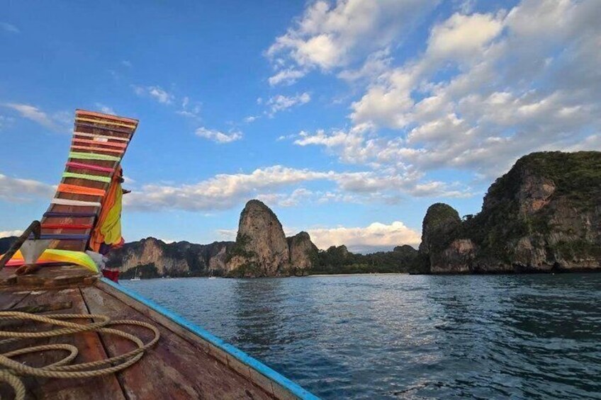 A boat with a colorful striped chair and ropes on deck, surrounded by clear blue water and limestone karsts under a partly cloudy sky. 2