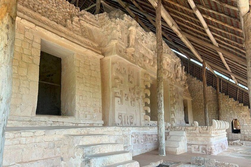 Une structure de pierre ancienne, ornée de sculptures et d’inscriptions, avec une porte partiellement ouverte et un toit en bois. 3