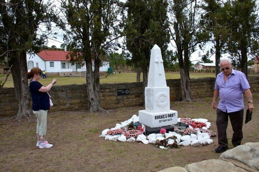 Een gedenkteken met een witte obelisk, bloemen en een plaquette. 2