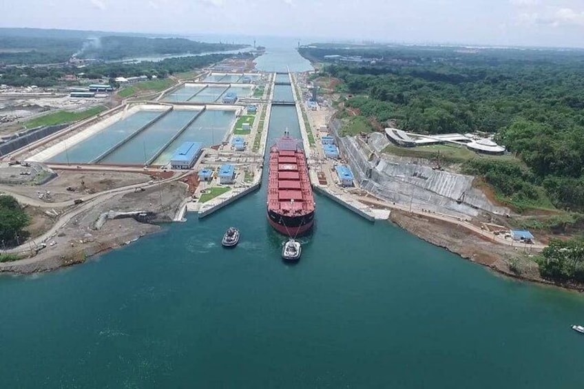 A large cargo ship navigating through a canal with multiple locks, surrounded by industrial buildings and greenery. 1