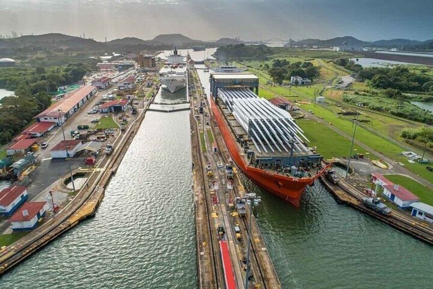 Un barco grande atracado en un puerto con esclusas, rodeado de edificios industriales y un paisaje verde. 1