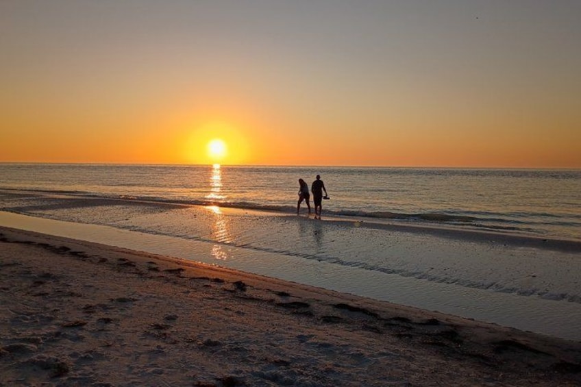 A sunset over a beach with footprints and two people walking. 5