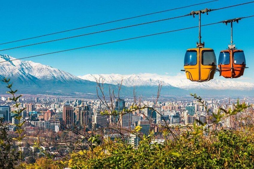 Une vue urbaine avec une chaîne de montagnes en arrière-plan, deux téléphériques et un ciel bleu dégagé. 1