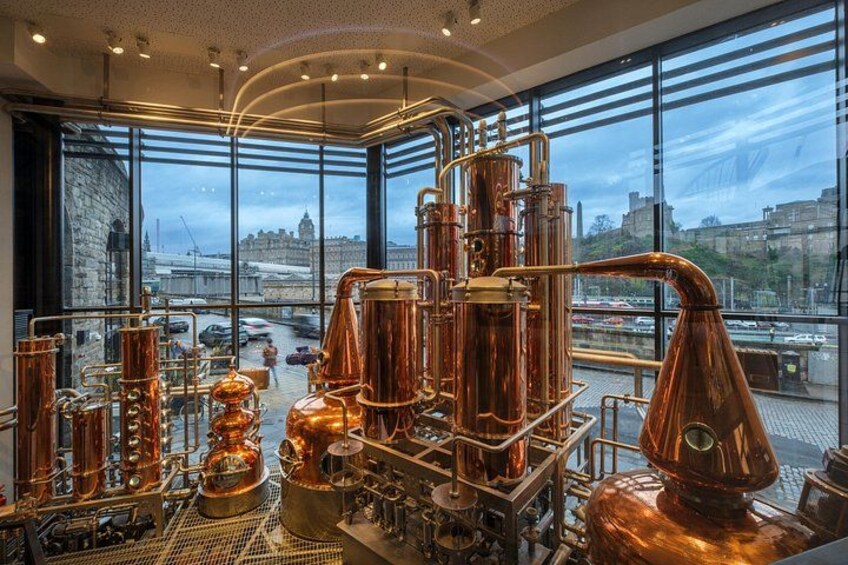 A distillery with copper stills and a city view through large windows. 1