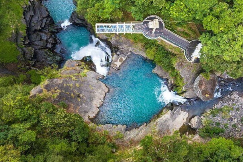 A waterfall cascading over rocks, surrounded by lush greenery, with a viewing platform and bridge. 1