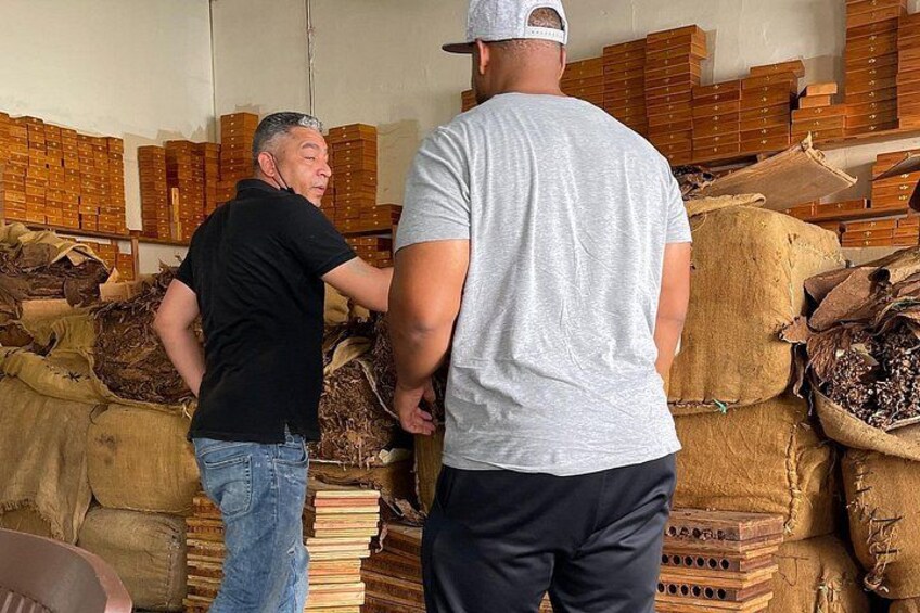 Two men standing in a warehouse with stacks of wooden boxes and sacks. 5