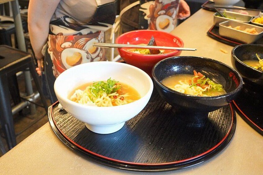 Un bol de nouilles ramen, accompagné d’un bol rouge et de baguettes, d’un bol noir contenant des légumes et d’un bol rouge avec une cuillère. 3