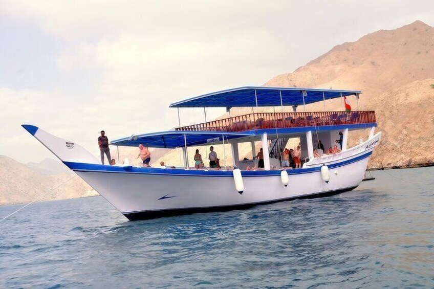 A boat with passengers on a calm sea, surrounded by rocky hills. 1