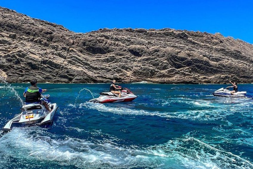 Tre jetski på et klart, blåt hav med klipper i baggrunden. 1