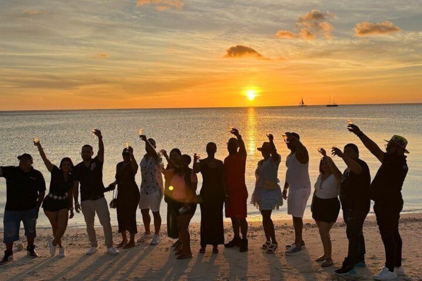 En gruppe mennesker står på en strand ved solnedgang, hvor solen er lavt på himlen. 2