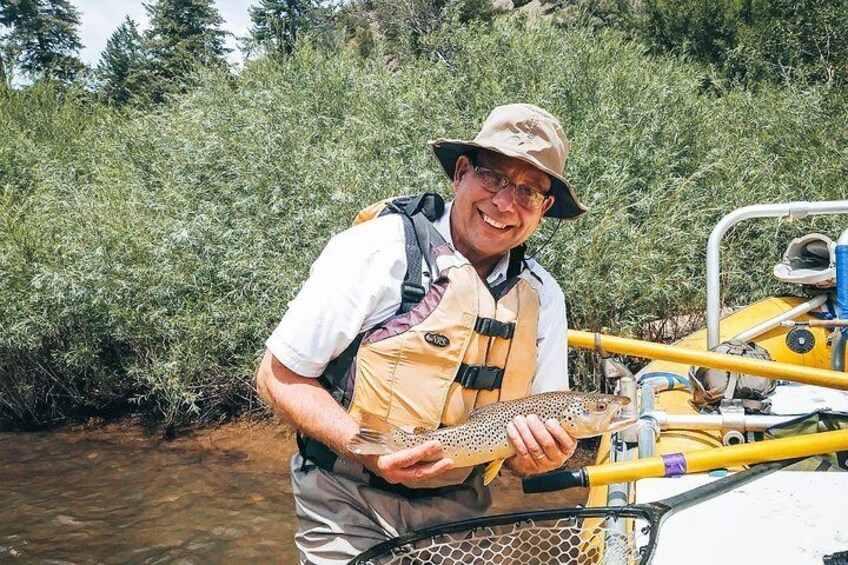 Un homme tenant un poisson près d’un bateau jaune dans une rivière bordée de verdure. 3