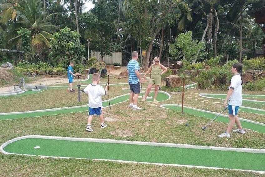 A mini-golf course with players and a lush, tropical background. 3