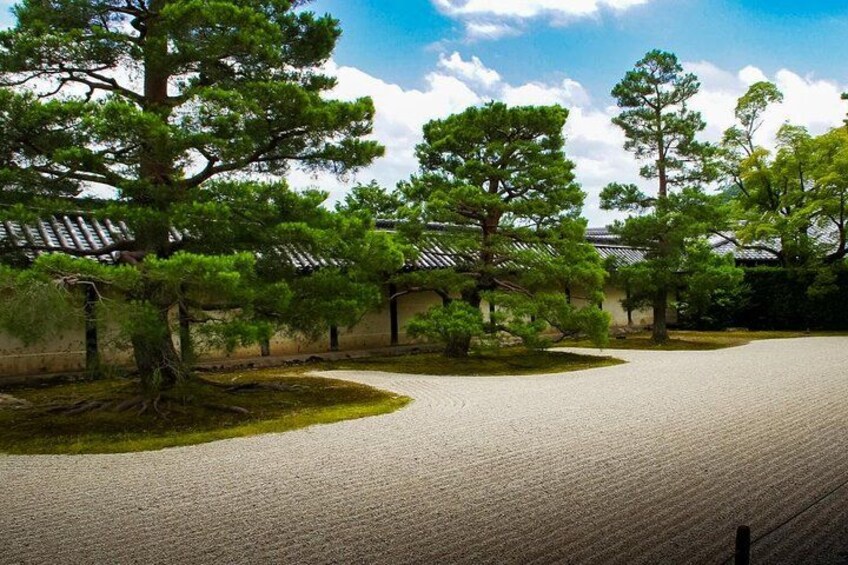 A traditional Japanese garden with a curved gravel path, pine trees, and a building with a tiled roof. 5