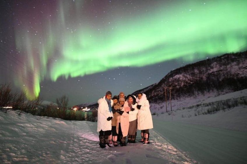 Un grupo de personas con abrigos blancos de pie en una ladera nevada bajo un cielo nocturno con la aurora boreal. 2