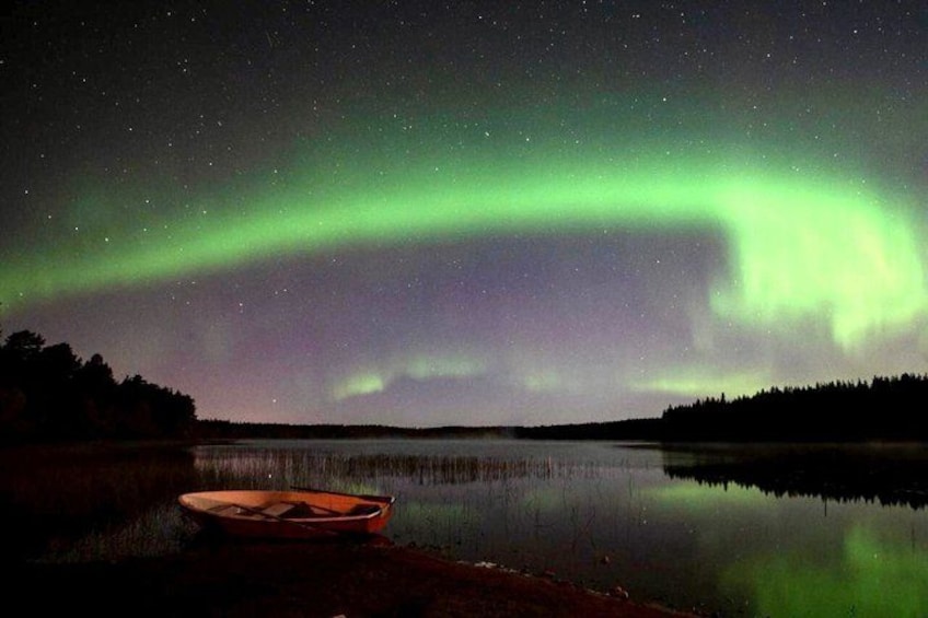 Un bote sobre un lago tranquilo de noche con auroras boreales en el cielo. 3