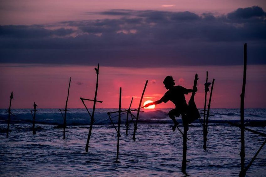 A silhouette of a person fishing at sunset with wooden poles in the water. 5