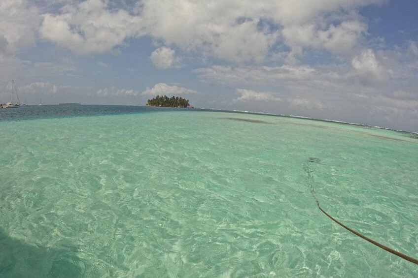 A clear turquoise sea, a small island with trees, and a distant shoreline. 2