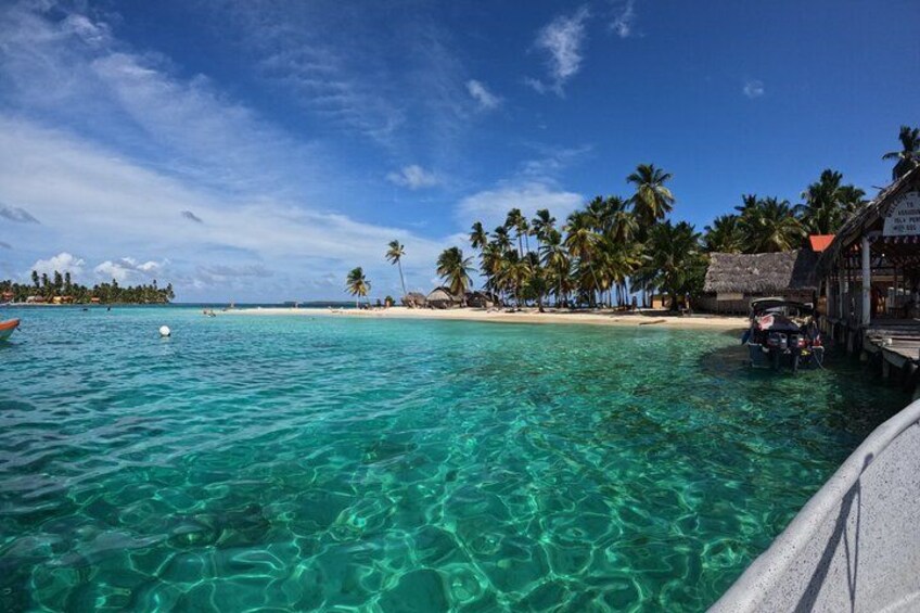 Ein klares türkisblaues Meer, ein sandiger Strand, Palmen und eine kleine Hütte mit einem Boot in der Nähe. 1
