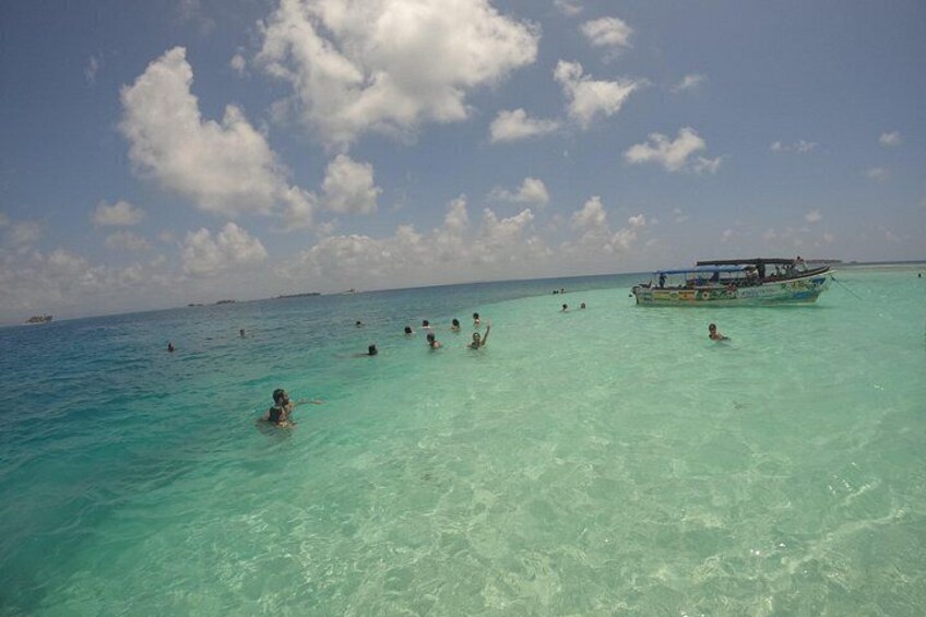 A clear turquoise sea with people swimming and a boat in the distance. 4