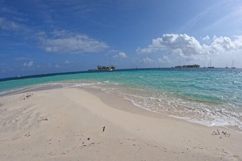 A beach with clear turquoise water, a sandy shore, and a small island with vegetation in the distance. 3