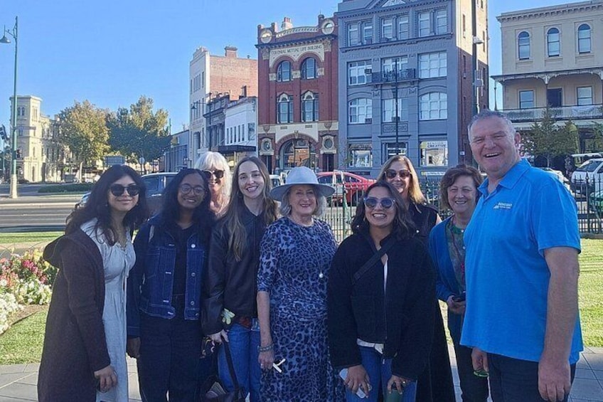 A group of people standing on a sidewalk with historic buildings in the background. 2