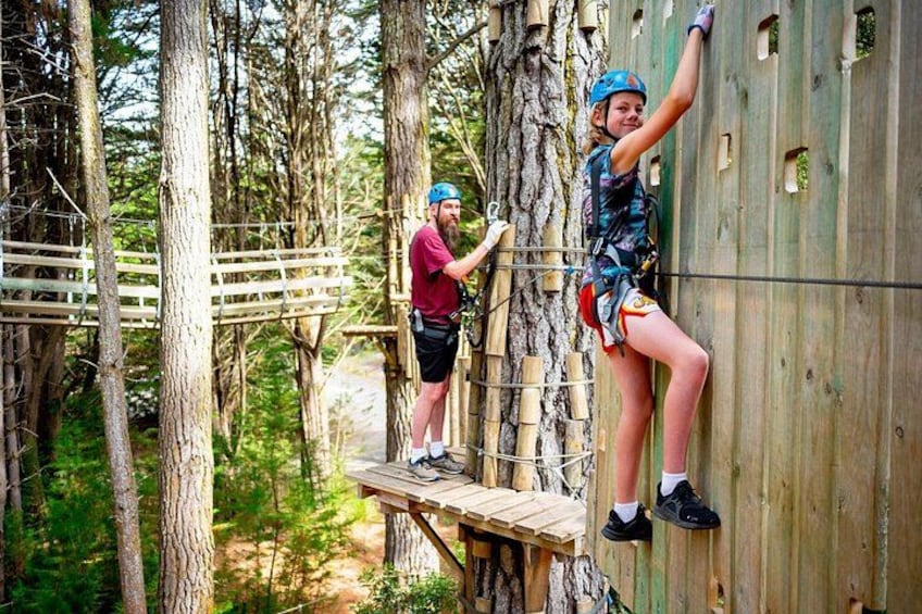 Two people climbing a wooden structure in a forest. 4