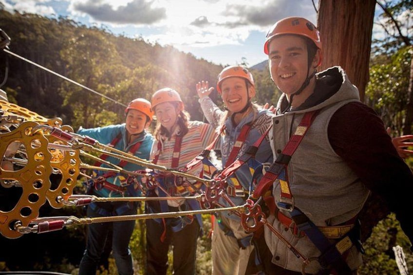 A group of people engaged in a zip-lining activity, wearing helmets and harnesses, with a forested landscape in the background. 3