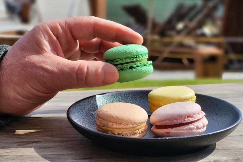 A hand holding a green macaron over a plate with three other macarons. 5