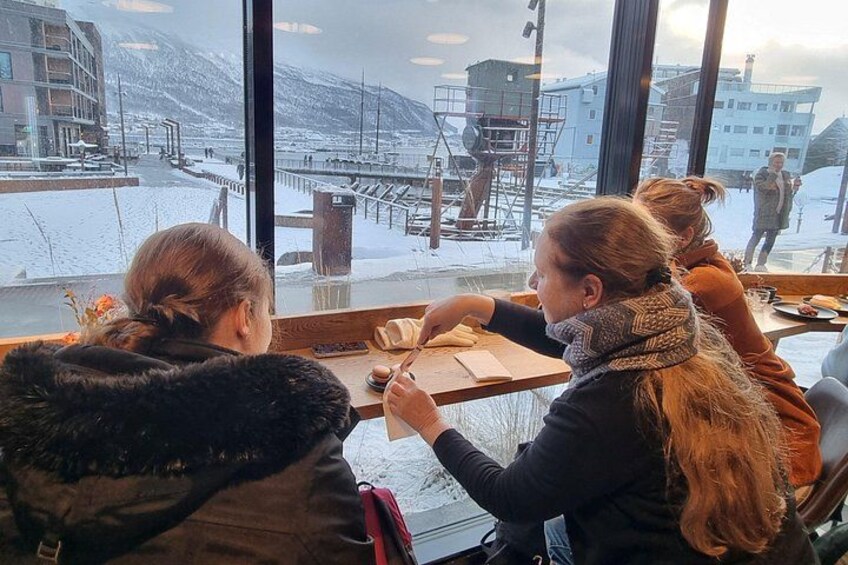 A group of people sitting at a table inside a building, looking out at a snowy outdoor scene with a dock and buildings. 4