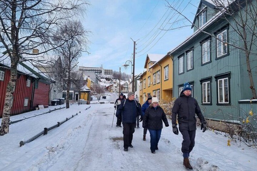 Una calle nevada con gente caminando, casas coloridas y árboles sin hojas. 2