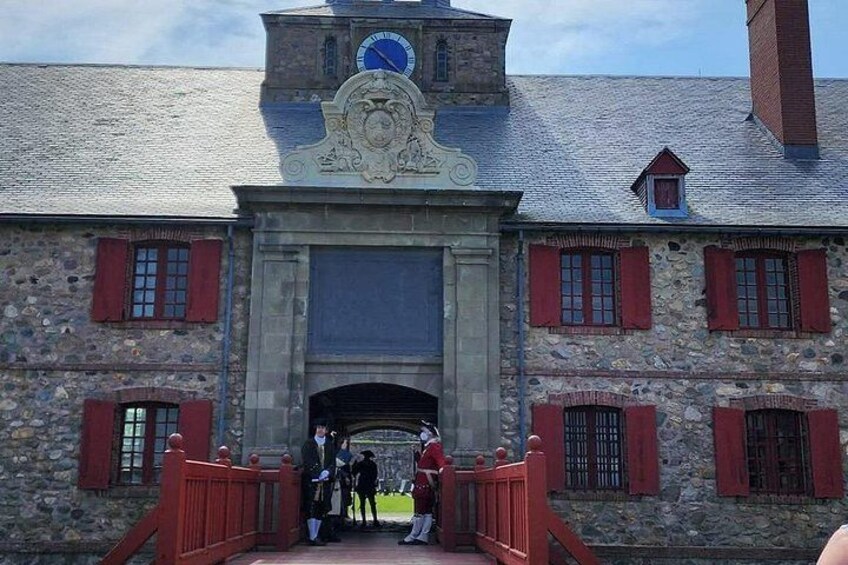 A stone building with a clock tower, red shutters, and a red bridge leading to the entrance. 5