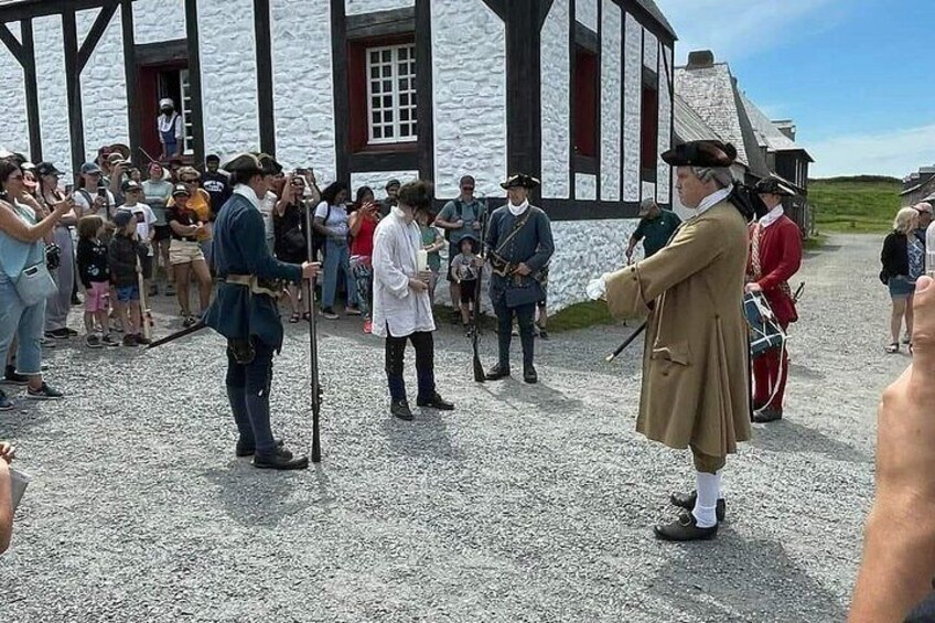 Een historische reconstructie met deelnemers in kleding uit die tijd, een toeschouwend publiek en een gebouw met zwart-witte vakwerkbekleding. 5