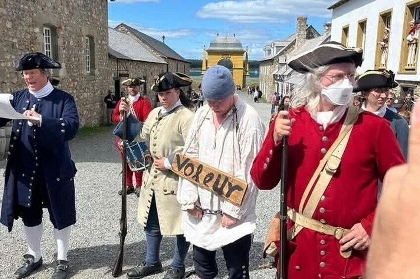 People in historical costumes, a sign with 'VORLEY', and stone buildings in a town square. 2
