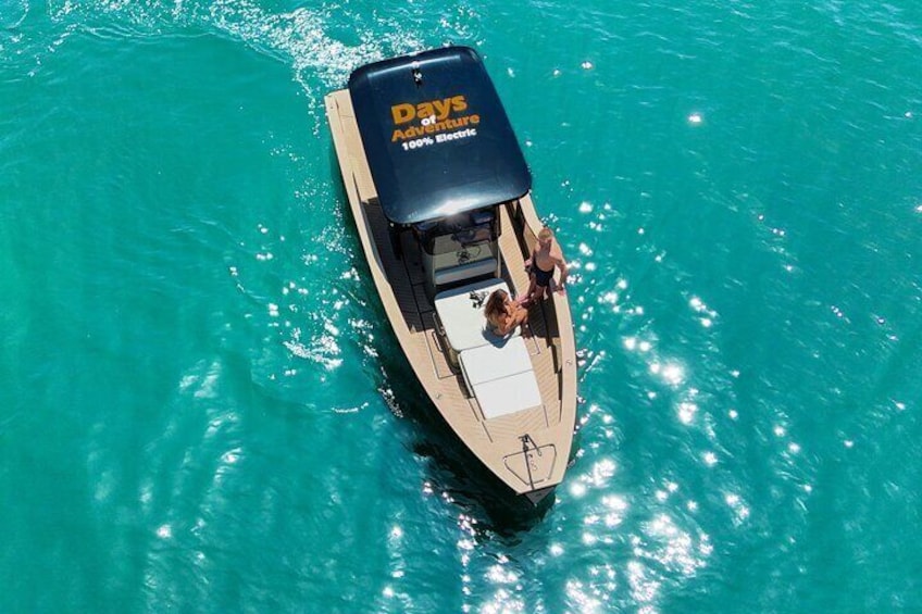Un barco con toldo azul que dice "Days Adventurous 100% Electric" sobre aguas turquesas. 1