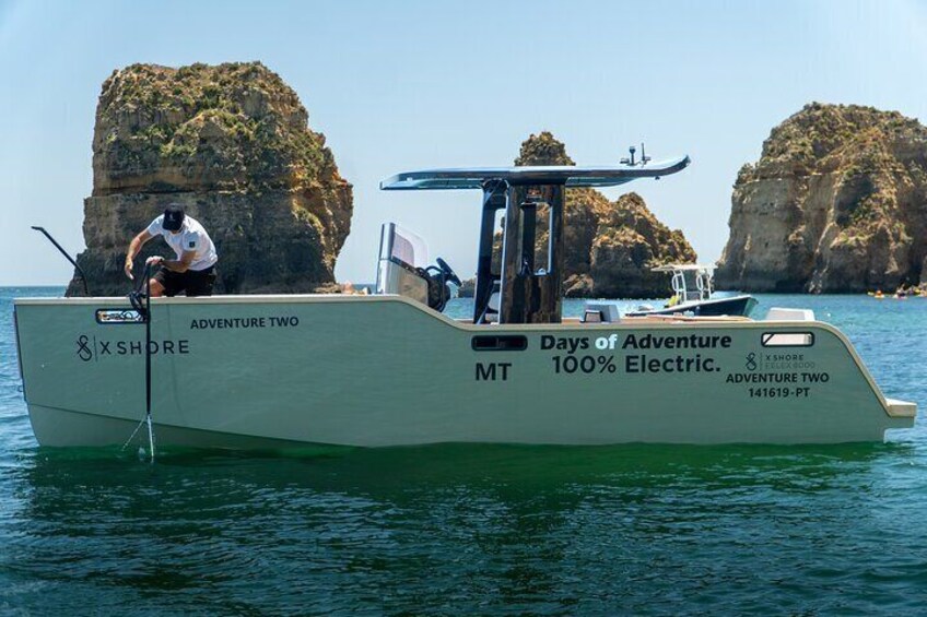 Un bote llamado 'Adventure Two' con la inscripción 'Days of Adventure 100% Electric' en su lateral, amarrado cerca de acantilados rocosos. 3