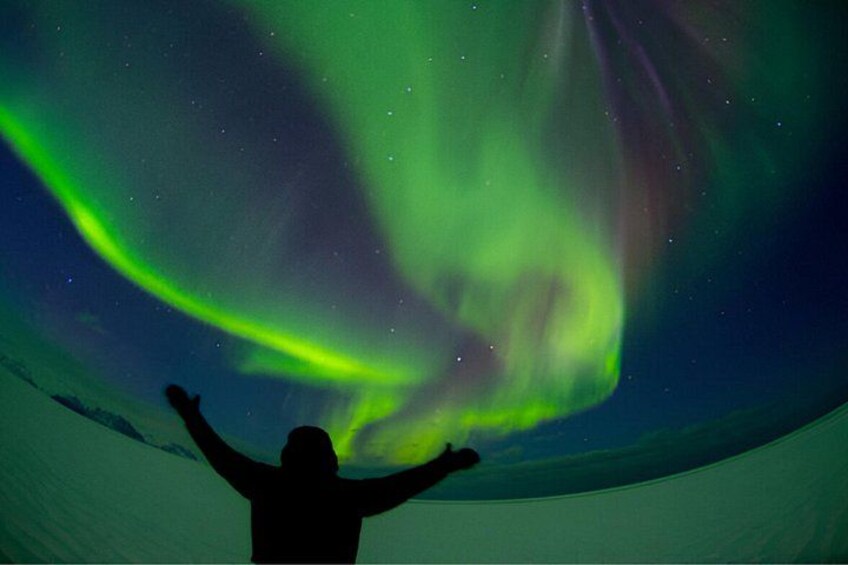 Una persona con los brazos levantados bajo la aurora boreal. 5