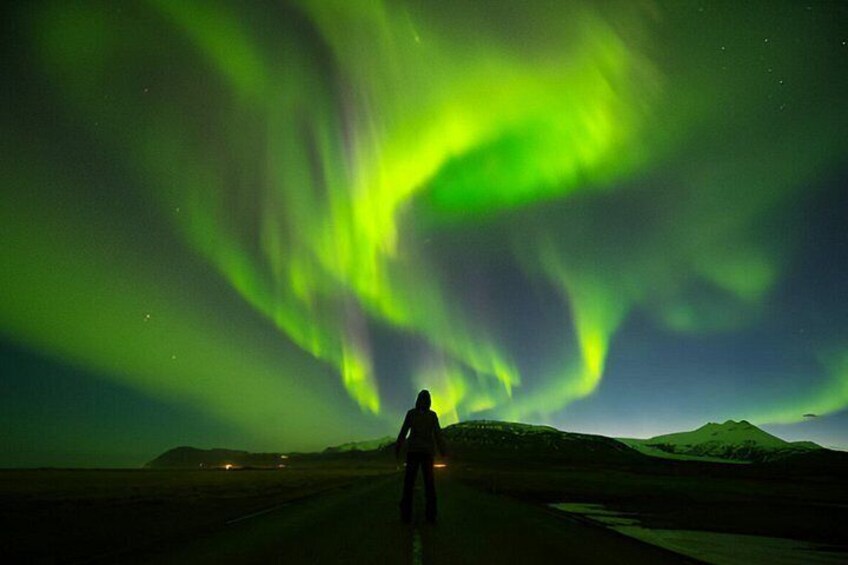 Una persona parada en una carretera bajo una exhibición verde de aurora boreal. 1