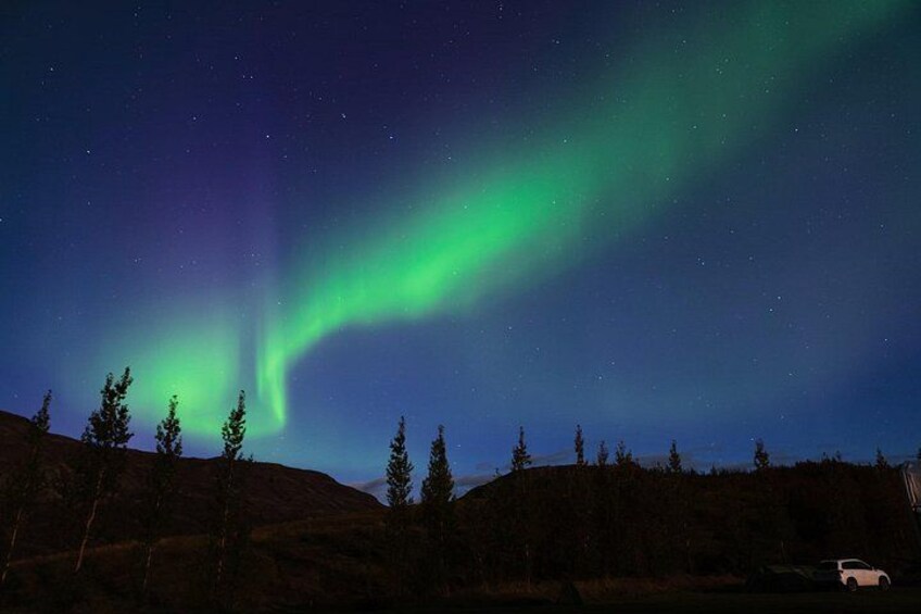 Nordlichter über einer bewaldeten Landschaft, im Vordergrund ein Auto. 4