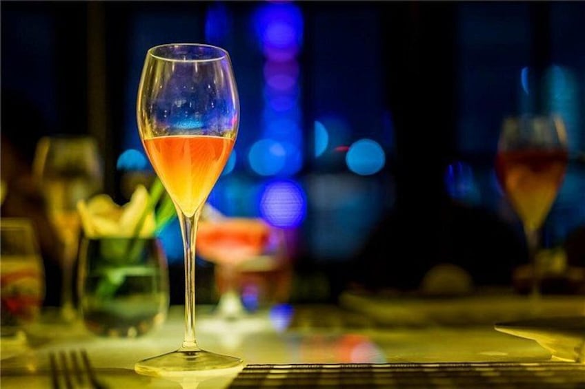 Ein Glas mit bernsteinfarbiger Flüssigkeit, möglicherweise ein Cocktail, auf einem Tisch vor unscharfem Hintergrund einer Bar. 1